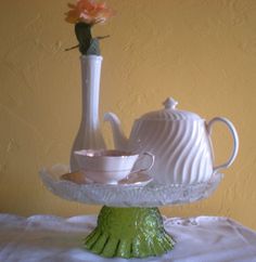 there is a tea set on the table next to a vase with a flower in it