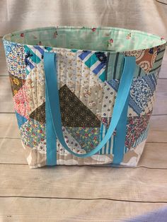 a multicolored patchwork tote bag with blue handles and straps sitting on a wooden surface