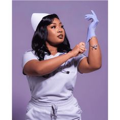 a woman in white scrubs her hands with blue latex gloves while posing for the camera