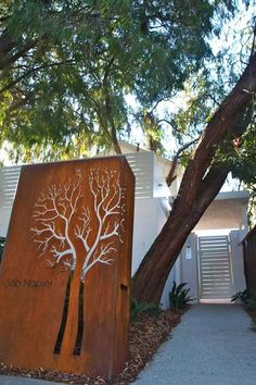 a large wooden sign sitting next to a tree on top of a cement walkway in front of a white building