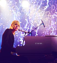 a woman sitting at a piano in front of a microphone on stage with fireworks behind her