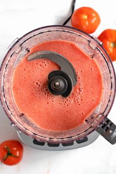 a blender filled with red liquid next to tomatoes