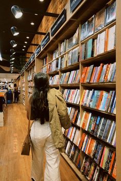 a woman is looking at books in a book store while another person walks past her