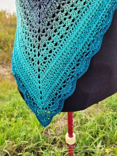 a woman wearing a blue and green crocheted shawl on top of a mannequin