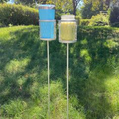 two blue and yellow containers sitting on top of a metal pole in the middle of a grass field