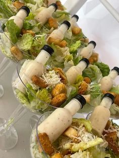 several glasses filled with salad and dressings on top of a white table next to each other