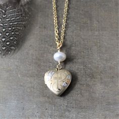 A lovely gold heart locket graces this necklace.  The vintage pendant has a cross in the center surrounded by white gold flowers; the back is plain.  The piece, hallmarked 14k gold fill on inside, has two compartments for photos in the interior.  The pendant is suspended from a creamy white freshwater pearl and is set on a new 14k gold filled chain.Locket 19x16mmNecklace length 18" (45cm) ✦All of our vintage lockets ship with complimentary insurance✦✤Our entire selection of lockets can be found Gold Cross Pendant Jewelry With Pearl Charm, Gold Jewelry With Pearl Charm Cross Pendant, Dainty Heart Pendant Jewelry With Vintage Charm, Dainty Locket Necklace For Memorial, Dainty Locket Necklace For Memorials, Spiritual Vintage Locket Necklace For Keepsake, Vintage Charm Necklace With Heart Pendant For Memorial, Heart Pendant Necklace With Vintage Charm For Memorial, Vintage Charm Necklaces With Heart Pendant For Memorial