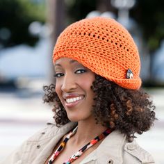 a woman wearing an orange crochet hat smiles at the camera while standing outside