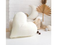 a white heart shaped pillow sitting on top of a table next to a basket with feathers