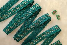 several pieces of green cloth with gold and white designs on them, next to some beads