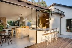 an outdoor kitchen and dining area with wooden flooring, white walls and ceiling lights