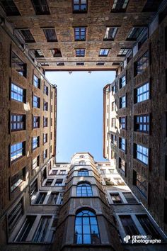 looking up at the sky from between two tall buildings in an alleyway with windows and balconies