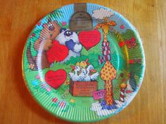 a paper plate with an image of animals and hearts painted on the side, sitting on a wooden table