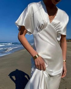 a woman standing on top of a beach next to the ocean wearing a white dress