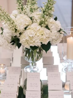 a vase filled with white flowers sitting on top of a table covered in place cards