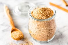 a glass jar filled with brown sugar next to a wooden spoon on top of a white counter