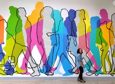 a woman is standing in front of a colorful wall with people painted on the side