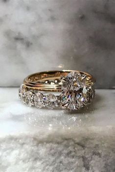 two gold wedding rings sitting on top of a marble counter next to another ring that has a diamond in the middle