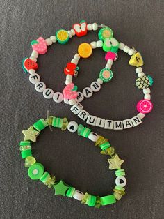 two bracelets with beads and letters on them sitting on a gray surface, one has a name tag in the middle