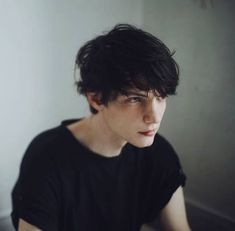 a young man sitting in front of a white wall