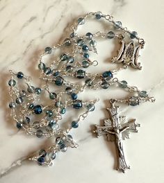 Wire-wrapped Catholic Rosary with Ave Marie beads of 6mm Bermuda Blue crystal beads and Pater Noster beads of 8mm Bermuda Blue crystal beads, capped in pewter and a 3mm clear crystal bead. The Sunburst Crucifix is made of pewter and 2 inch in length. There is a pewter Miraculous Medal/Ave Maria centerpiece. Each bead was wire-wrapped by hand with German wire to ensure a rosary that will last. The Rosary is 27 inches long. Each of my rosaries come with a lifetime guarantee - return for free repai Silver Rosary With Faceted Beads For Gift, Silver Rosary With Faceted Beads As Gift, Handmade Silver Rosary With Round Beads, Bohemian Silver Rosary For Jewelry Making, Handmade Silver Rosary For Healing, Silver Bohemian Rosary With Round Beads, Blue Crystal Beads, Catholic Rosary, The Rosary