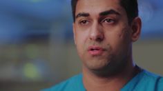 a close up of a man in scrubs looking off to the side with a serious look on his face