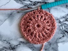 a crocheted object is sitting on a marble surface next to a knitting needle