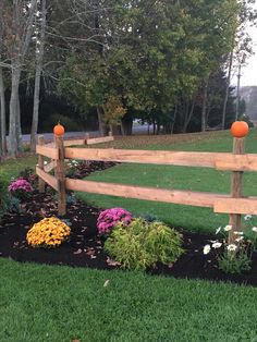 a wooden fence surrounded by flowers and plants on the grass in front of some trees