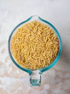 a glass bowl filled with yellow pasta on top of a marble countertop next to a white wall