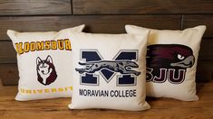 three pillows with university logos on them sitting on a table in front of a wood paneled wall