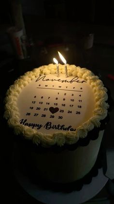 a birthday cake with a calender on it and two lit candles in the middle