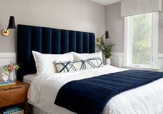 a bed with white and blue sheets in a bedroom next to a large window on the wall