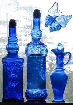 three blue glass vases sitting on top of a table next to a butterfly flying over them