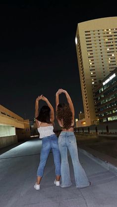 two women standing in the middle of a parking lot at night with their hands up