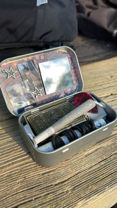 an open tin with some items in it on a wooden table next to a backpack