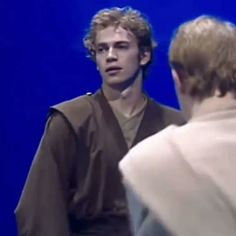 a man standing next to a woman in front of a blue background wearing a cape