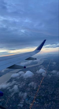 the wing of an airplane as it flies through the sky with clouds and buildings below