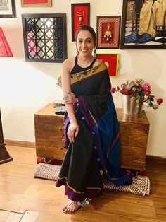 a woman in a black and blue sari sitting on a wooden floor next to a dresser