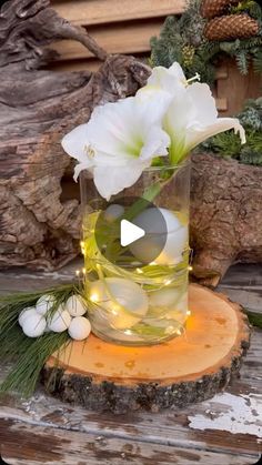 a vase filled with white flowers sitting on top of a wooden table next to a log