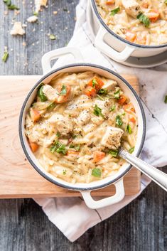 two pots filled with chicken noodle soup on top of a wooden cutting board