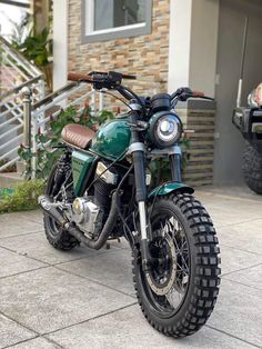 a green motorcycle parked on top of a sidewalk next to a building with stairs in the background