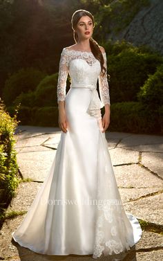 a woman in a white wedding dress standing on a stone path with trees and bushes behind her