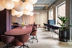 a large conference room with round tables, chairs and plant in the center is lit by globe lights