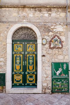 two green and yellow doors on an old stone building with decorative decorations around the door