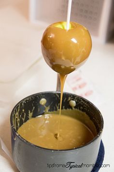 an apple being dipped with caramel sauce in a metal bowl on a table top