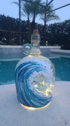 a glass bottle that has some lights in it and is sitting next to a pool