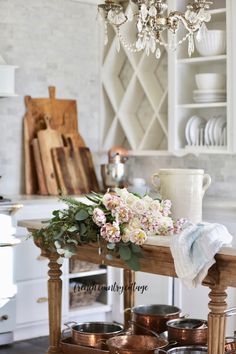 a chandelier hanging from the ceiling above a wooden table filled with pots and pans