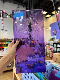 a person holding up a purple piece of art in a store with other items on the shelves