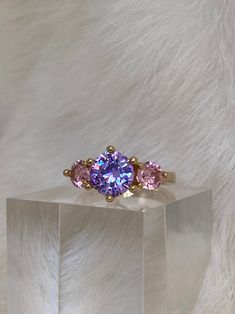 The Lilac Lilly Ring is a dashing doll! This beaut features a central 8mm lilac cubic zirconia crystal hugged between two 4mm pink brilliant cut CZ stones on a smooth dainty band. Layer this belle with these pieces for an flawless look: - The Bluebell Ring - The Mini Lavender Heart Necklace - The Trixi Crystal Bar Earrings Available in 24K gold or rhodium plating over steel Patent plating & sealant technology to ensure durability and long lasting wear Made in Los Angeles, CA | Nickel & Lead Free Lavender Ring, Fairytale Decor, Purple Stone Rings, Lavender Heart, Pretty Jewelry Necklaces, Dainty Band, Cute Engagement Rings, Purple Amethyst Ring, Purple Rings