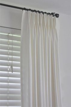 white curtains hanging in front of a window with blinds pulled up to the side and closed